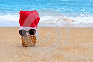 Picture of  pineapple wearing sunglass and Santa Claus hat on the tropical beach. New Year and Christmas concept. Happy New Year