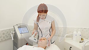 Picture of pretty beautician doing rf-lifting procedure for woman laying down in a beauty salon
