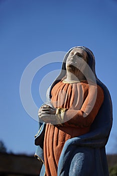 Picture with selective focus of a statue of the blessed virgin mary praying in front of the blue sky