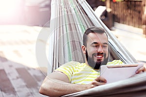 Picture showing happy man resting on hammock with tablet