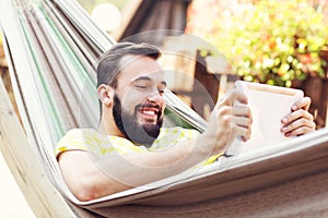 Picture showing happy man resting on hammock with tablet