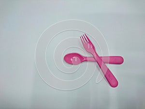 The picture shows a pink spoon and fork plastic on a white background.