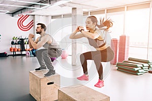 A picture of slim and well-built young man and woman doing jumps on platform. It is a hard exercise but they are doing