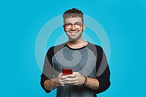 Picture of smiling bearded man with eyeglasses writing message on smartphone over blue background