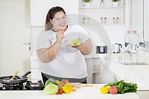 Smiling fat woman eats a healthy salad in kitchen