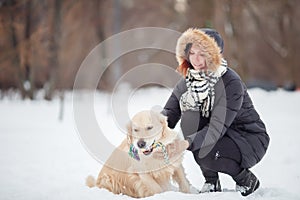 Picture of smiling woman squatting next to labrador with toy in teeth in winter park