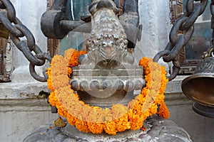 Statue with a garland made with orange flowers at the Boudhanath Stupa, Kathmandu, Nepal