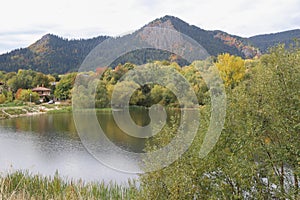 A picture of a stunning autumnal landascape with lots of colors, trees and a romantic lake surrounded by high mountains