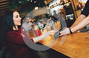 A picture of stunning girl sitting close to barman and paying for her order. She gives a credit card to barman to pay