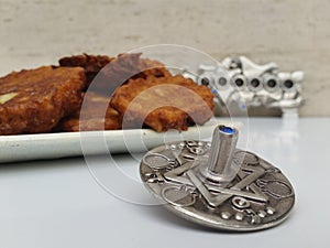 A plate full of Hannukah potato latkes fritters with a silver dreidel on a white table with a silver chanukiah in the background