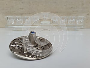 A silver dreidel on a white table with a glass chanukiah in the background