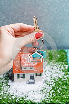 Picture of toy house with falling snow and hands with key