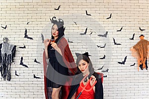 Picture of two emotional young women wearing witch halloween costumes on party over background decorated for Halloween