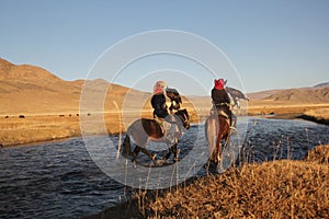 Picture of two horseriders in a river surrounded by a deserted valley with hills on the background