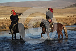 Picture of two horseriders in a river surrounded by a deserted valley under a blue sky