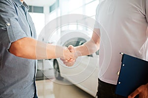 Picture of two young men shaking hands in front of white car. They made an agreement. Customer and seller works together