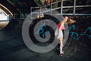 A picture of well-built rollerblaider riding backwards. She is looking back careful. Girl is smiling. Her hair is waving.