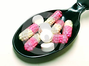 A picture of white tablets and red capsules on a black spoon ,