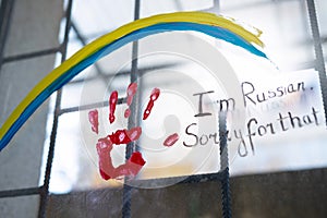 Picture on window with bars of Ucranian flag as a rainbow sign and a red handprint with an inscription of sorry i am