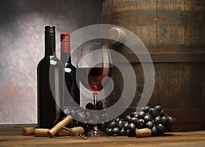 Picture with wine bottles, wineglass of red wine, wooden old barrel and dark grape