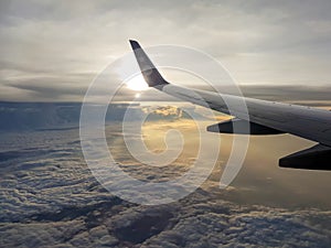 Picture of wing of air plane flying above the clouds with sun from window