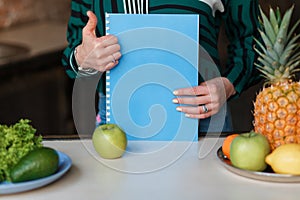Picture of woman with fruits and notebook showing thumbs up. Close shot no face