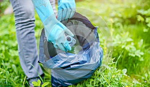 Picture of woman in rubber gloves picking up dirty plastic bottle in bag on green lawn