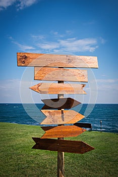 Picture of wooden direction signpost in front of the sea and grass