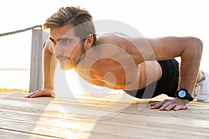 Picture of a young athletic man doing push ups outdoors