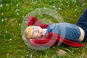 Picture of young beautiful blond man laying on green grass among