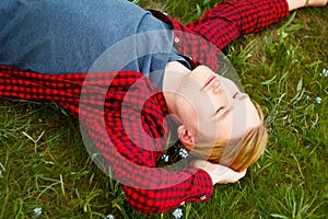 Picture of young beautiful blond man laying on green grass among