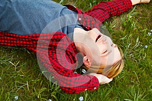 Picture of young beautiful blond man laying on green grass among