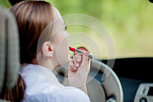 Picture of young businesswoman doing makeup while driving a car in the traffic jam