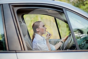 Picture of young businesswoman doing makeup while driving a car in the traffic jam