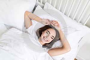 Picture of young happy woman dressed lies on bed at home indoors.
