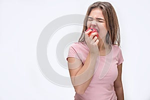 Picture of young woman biting piece from apple. She shrinks. Iolated on white background.