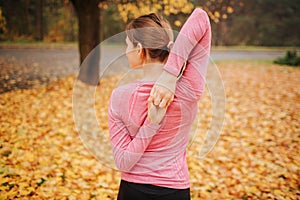 Picture of young woman stands in autumn park and look to left. She stretches hands. Woman keep them together behind back.