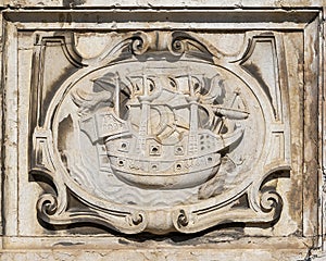 Ancient engraved stone relief in Lisbon with a sailboat and two ravens/ photo