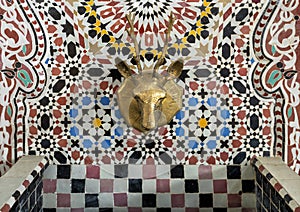 Closeup of a mosaic fountain with geometric Arabic design and stag head faucet on display at Art Naji in Fez, Morocco.