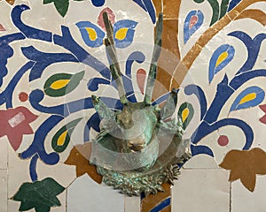 Closeup of a mosaic fountain with geometric Arabic design and stag head faucet on display at Art Naji in Fez, Morocco.