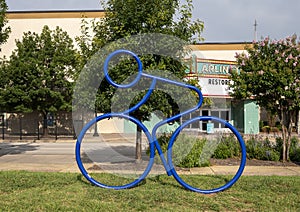 Tubular steel sculpture of a person riding a bike in the grass near the historic Vandergriff Office Building in Arlington, Texas.