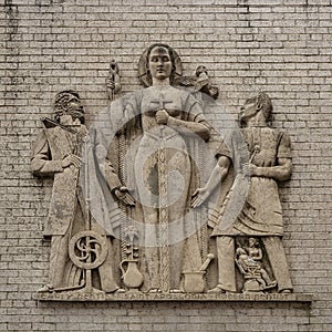 Weathered old stone relief featuring Saint Apollonia flanked by a modern dentist and an early dentist in downtown Tulsa, Oklahoma.