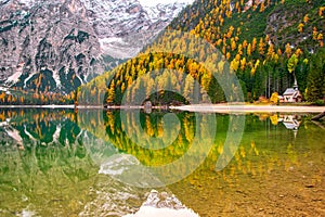 Picturesque autumn scenery of historic chapel and colorful trees reflected in Lago di Braies in the Dolomites, Italy