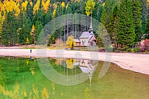 Picturesque autumn scenery of historic chapel reflected in water of Lago di Braies in the Dolomites, Italy