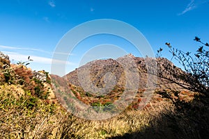 Unzen Nita Pass trail with rocky volcano peak, clear blue sky and colorful trees in Unzen-Amakusa National Park, Japan photo