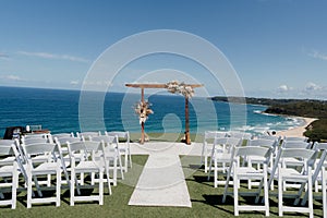 Picturesque beach wedding with white folding chairs and an arch adorned with colorful flowers