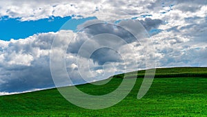 Picturesque cloudscape. Blue sky with clouds over a green field with grass. Windows desktop wallpaper example. Cloudy weather with