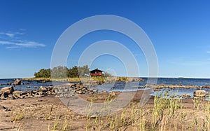 Picturesque coastal landscape on the Baltic Sea with a small red cottage on an island behind a sandy beach under a blue sky