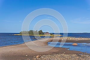 Picturesque coastal landscape on the Baltic Sea with a small red cottage on an island behind a sandy beach under a blue sky