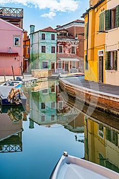 Picturesque colorful idyllic scene with a boats docked on the water canals in Burano Venice Italy. Water reflection